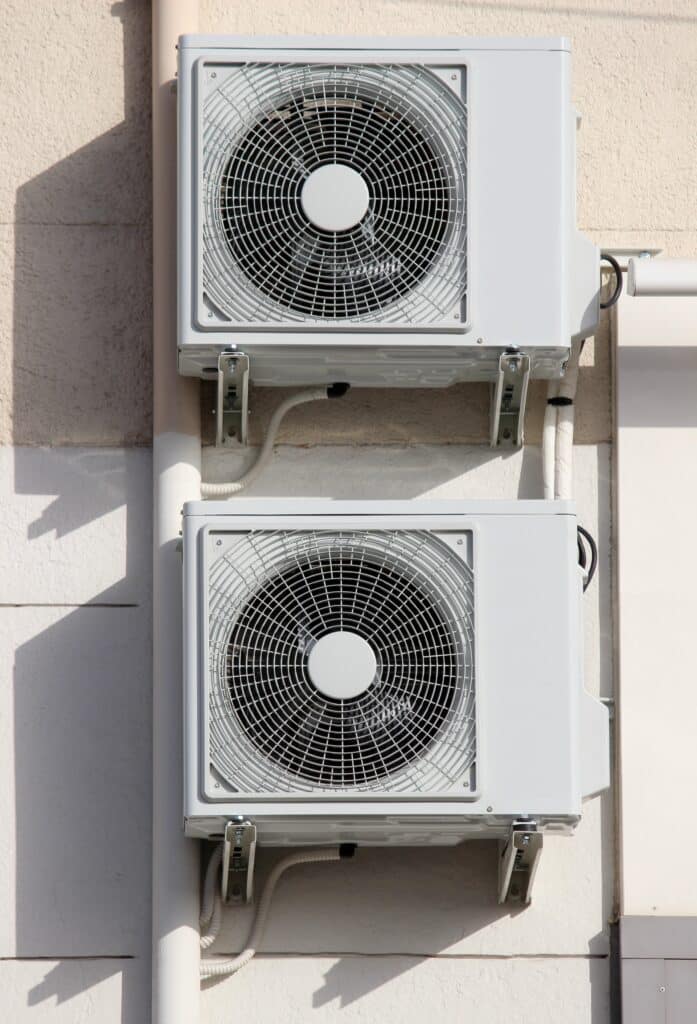 Climatiseurs Extérieurs Muraux Japonais avec Câblage Deux unités extérieures de climatiseur blanches superposées, fixées à un mur texturé beige clair sous un éclairage solaire intense.