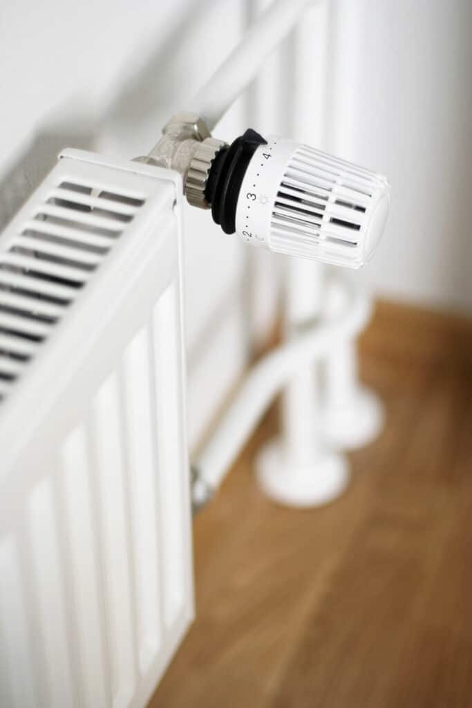 Réglage thermostatique radiateur : mode nuit sur 2 Gros plan sur une vanne thermostatique blanche réglée sur le chiffre 2 (mode nuit/lune) sur un radiateur blanc, avec un sol en bois en arrière-plan flou.